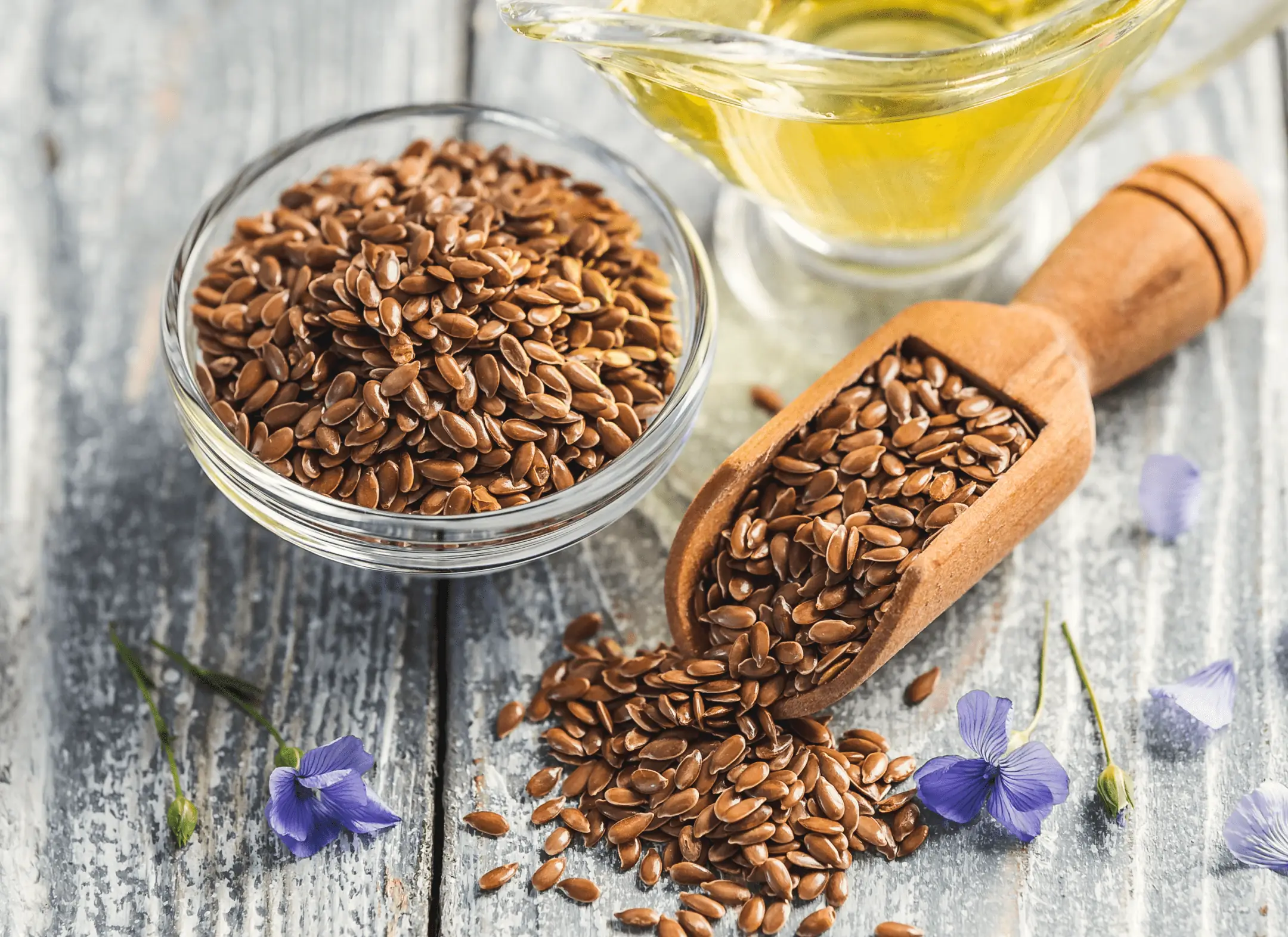 Flaxseeds in a glass bowl and wooden scoop with flaxseed oil