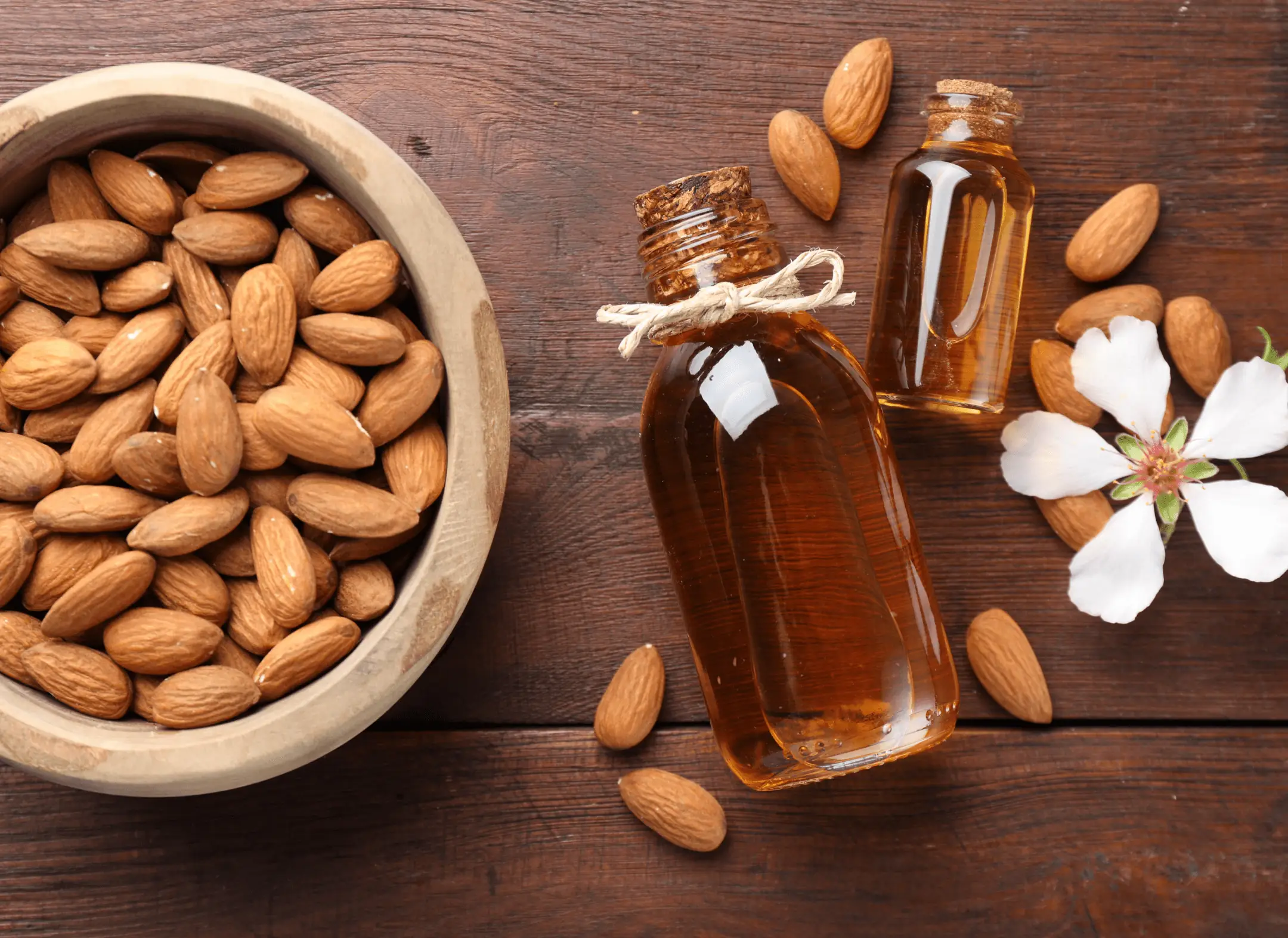 Almonds in a wooden bowl beside bottles of almond oil
